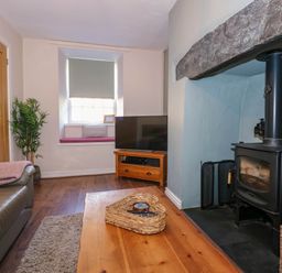 A living room with a wood stove and a television on a wooden stand at Yr Hen Dy Capel in Blaenau Ffestiniog