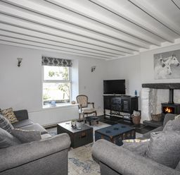 A living room with gray sofas a window a wood burning stove and a television at Glyn Morfa in Harlech
