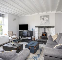 A living room with grey sofas a fireplace and a television at Glyn Morfa in Harlech