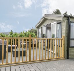 An outdoor deck with wooden railing and wicker chairs outside a cabin with glass doors at The Maple in Cloughton