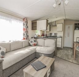 A living room with an L-shaped sofa and patterned curtains next to an open kitchen and dining area at The Maple in Cloughton