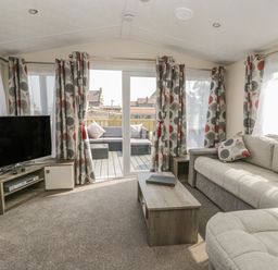A living room with a sofa a coffee table a television and curtains on windows at The Maple in Cloughton