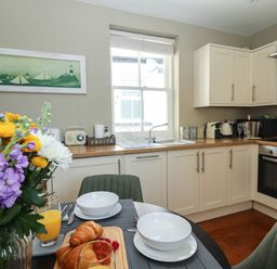 A kitchen with beige cabinets a window and a dining table set with bowls croissants and flowers at Gavel Cottage in Whitby