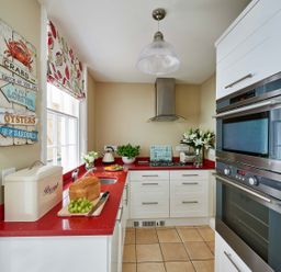 A kitchen with red countertops white cabinets built in oven bread box and a window at Harbour House in Whitby