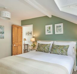 A bedroom with a bed against a green wall with two pillows and two framed pictures two bedside tables with lamps and flowers and an open wooden door at Harbour House in Whitby