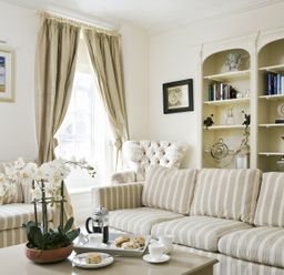 A sitting room with striped sofas, a coffee table with tea and scones, bookshelves, and curtains at Albany House Whitby
