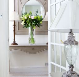 A hallway with a console table holding a vase of flowers and a lamp with a mirror above the table at Albany House Whitby