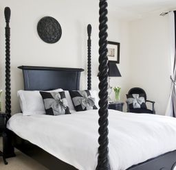 A bedroom with a black four-poster bed white bedding black and silver decorative pillows two black nightstands with silver lamps and flowers black chair with pillow and window with curtains at Albany House Whitby