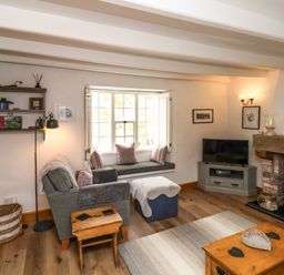 A living room with a gray armchair ottoman and wooden tables a TV on a corner cabinet and a fireplace at The Cottage in Sandsend