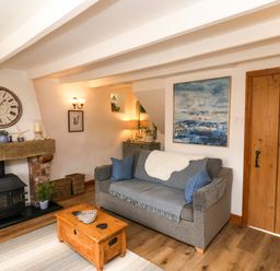 A living room with a gray sofa and blue cushions a wooden coffee table and a wood burning stove at The Cottage in Sandsend