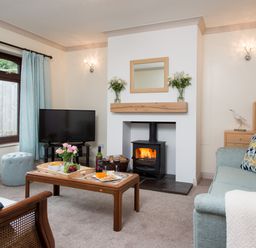 A living room with a wood burning stove and TV and a coffee table with wine and food at Seawinds in Robin Hood'S Bay