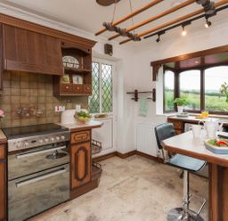 A kitchen with wooden cabinets a stove a table with chairs and a window overlooking greenery at Seawinds in Robin Hood'S Bay