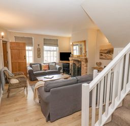 A living room with two grey sofas a wicker chair a wooden coffee table a fireplace and stairs at Rooftops Cottage in Whitby