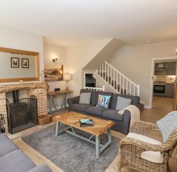 A living room with two gray sofas a wicker chair a wooden coffee table a fireplace and stairs at Rooftops Cottage in Whitby
