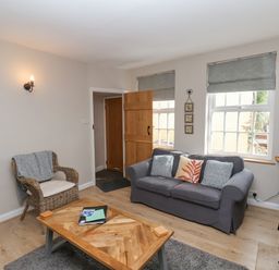A living room with a gray sofa, a wicker chair, a wooden coffee table, and windows with gray blinds at Rooftops Cottage in Whitby