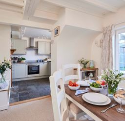 A dining table set with plates bowls and wine in a room with a kitchen in the background at Rigg Cottage Sandsend