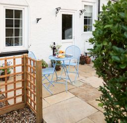 An outdoor patio with a blue table and chairs set near a white house with windows and a door at Rigg Cottage in Sandsend
