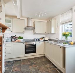 A kitchen with beige cabinets a stainless steel oven and extractor a granite countertop and slatestone floor at Rigg Cottage in Sandsend