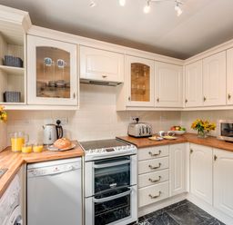 A kitchen with white cabinets a stove a dishwasher a washing machine a microwave a toaster a kettle flowers and orange juice at Esk View Cottage in Grosmont