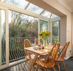 A dining area with a wooden table and four chairs next to glass doors overlooking trees at Esk View Cottage in Grosmont