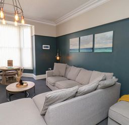 A living room with a sectional sofa coffee table and round dining table near bay windows at Church View in Whitby