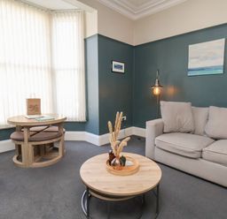 A sitting room with a beige sofa a round coffee table and a small dining table near a window at Church View in Whitby