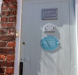 A grey wooden door with three signs including Albany Cottage and Yorkshire Coastal Cottages at Albany Cottage in Whitby