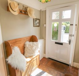 An entrance hall with a white door wooden bench with cushions hats hanging on hooks and a radiator at Arden House Whitby