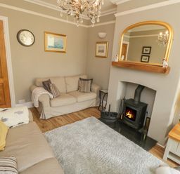 A living room with two sofas a wood burning stove a mirror above the fireplace and a wooden side table with a vase of flowers at Arden House Whitby