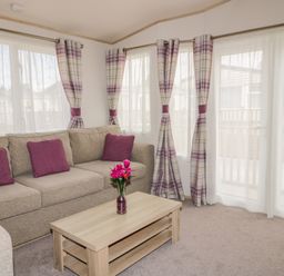 A living room with a beige sofa and purple cushions and a wooden coffee table with a vase of pink flowers at The Hideaway in Cockermouth