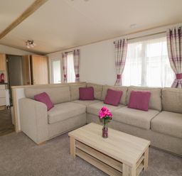 A living room with a beige corner sofa with purple cushions and a wooden coffee table with a vase of flowers at The Hideaway in Cockermouth
