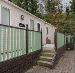An exterior view of a beige mobile home with green and brown wooden railing and steps leading to the entrance at The Hideaway in Cockermouth