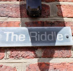 A metal sign with the text The Riddle mounted on a brick wall at The Riddle in Whitby