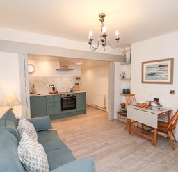 A living area with a blue sofa and a small dining table with two wooden chairs next to an open kitchen with green cabinets at The Riddle in Whitby
