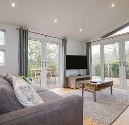 A living room with gray sofas wooden coffee table wall-mounted TV and glass doors opening to a deck at 6 Valley View in Lanreath