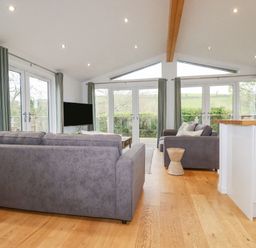 A living room with gray sofas a wooden stool a flat screen tv and large windows at 6 Valley View in Lanreath