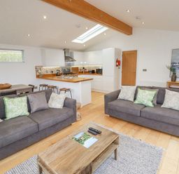 An open plan living area with two sofas a wooden coffee table a dining table and a kitchen at 6 Valley View in Lanreath