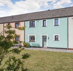 A row of terrace houses with pastel-colored walls a green door and benches with a grassy yard in front at Granary Cottage in Pembroke