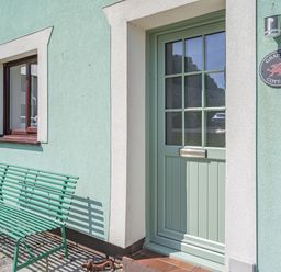 A green bench next to a green door and a window on a light green wall at Granary Cottage in Pembroke