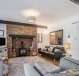 A living room with a brick fireplace a black sofa and a gray armchair at Granary Cottage in Pembroke
