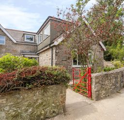 Stone house with multiple windows and a red gate with bushes and trees around at Gorwel in Moelfre