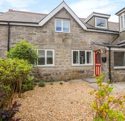 A stone exterior house with a red door gravel front yard and green bushes at Gorwel in Moelfre