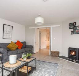 A living room with gray sofas and colorful cushions a glass coffee table with plants and a candle a fireplace and wall art at Gorwel in Moelfre