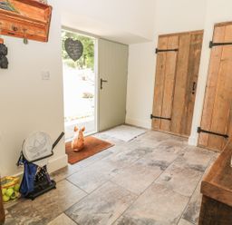 An entrance hall with a wooden bench a cushion two wooden doors a green door a coat rack a table with flowers tennis rackets and tennis balls at Sawmill Cottage in Belford near Bamburgh