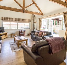 A living room with wooden beams leather sofas a coffee table and a television at Sawmill Cottage Belford near Bamburgh