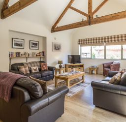 A living room with wooden beams leather sofas armchair and a wooden coffee table at Sawmill Cottage in Belford near Bamburgh