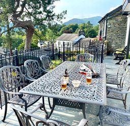 An outdoor patio with a metal table and eight chairs with drinks and a bowl on the table at Prospect House in Ambleside