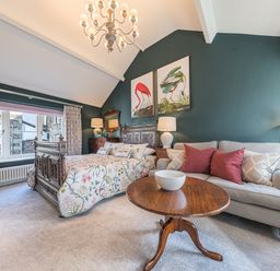 A bedroom with a wooden bed and floral bedspread a beige sofa with red and gray pillows and a round wooden coffee table in Prospect Cottage Loft Ambleside
