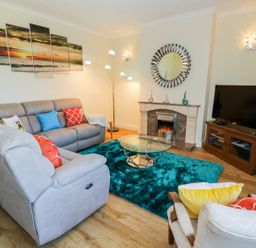 A living room with sofas a glass coffee table a fireplace a television and a multi panel sunset painting at Berwyn in Talybont