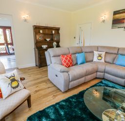 A living room with a grey sectional sofa with colorful cushions a wooden armchair with cushions a glass coffee table and a wooden cabinet at Berwyn in Talybont